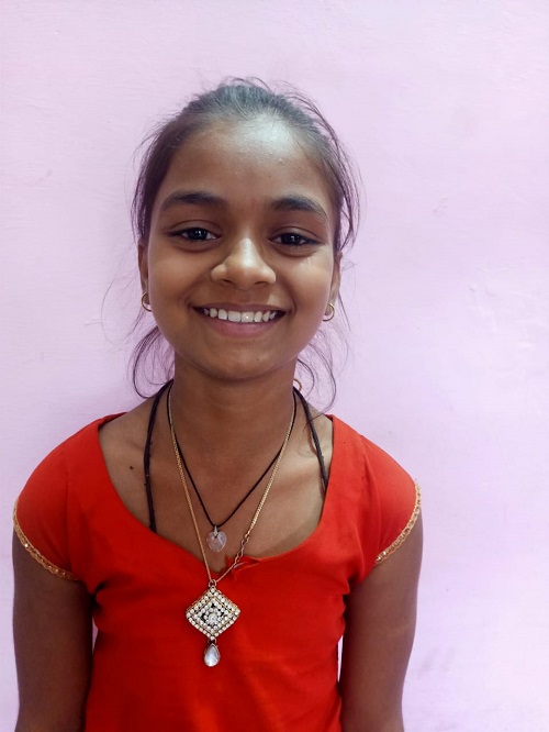 Young girl in India stands looking at the camera smiling.