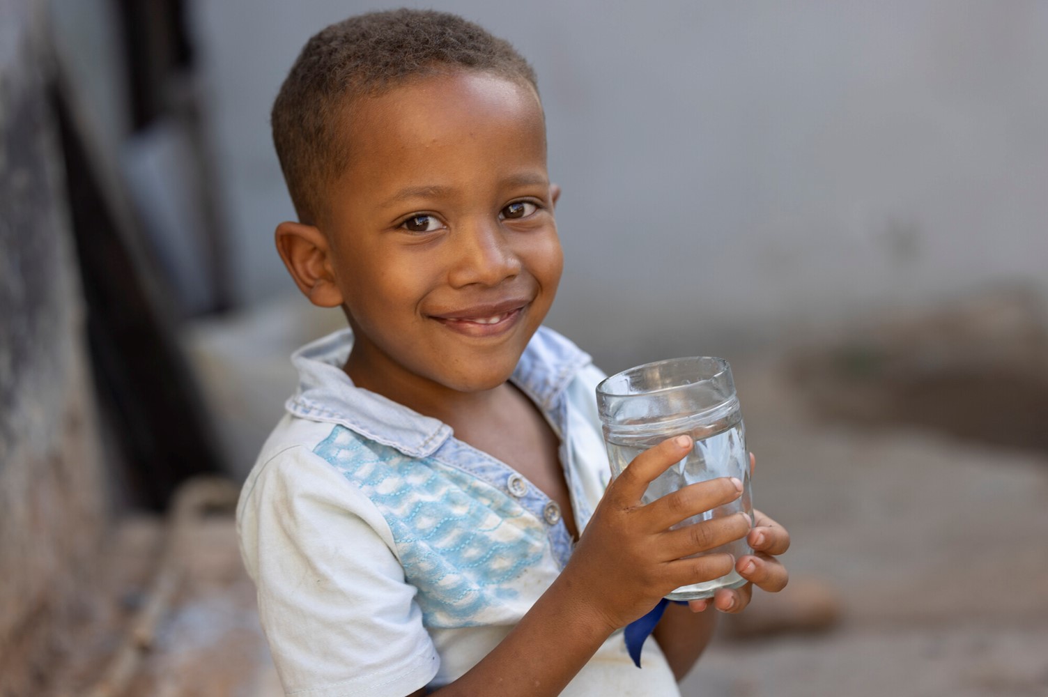 Smiling young boy holding a glass of clean water while standing outdoors.