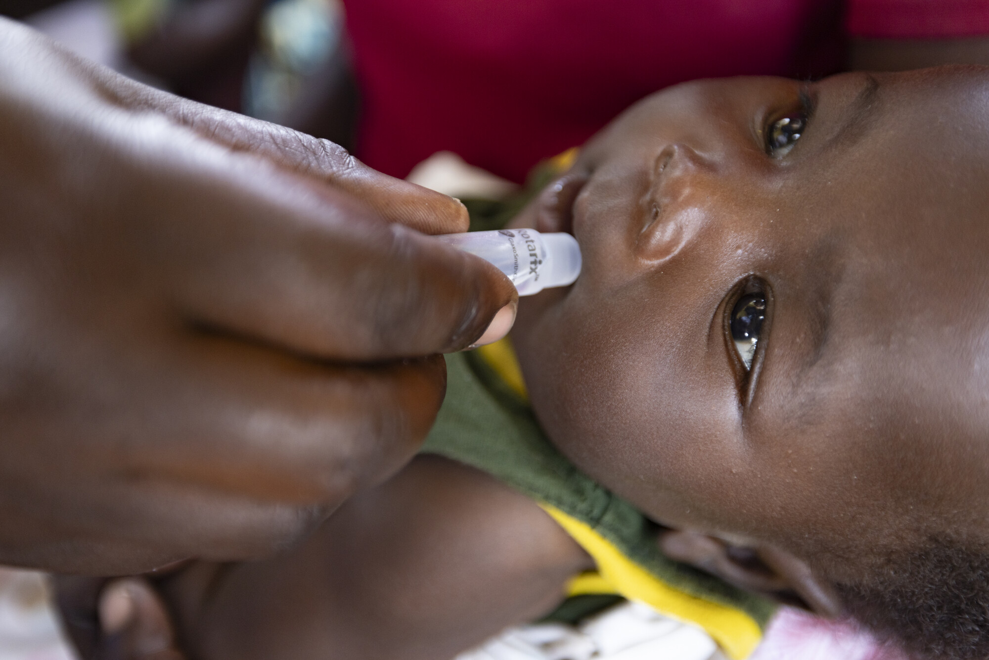 A baby lying down receives an oral dose of medicine from a caregiver’s hand, focusing on child healthcare.